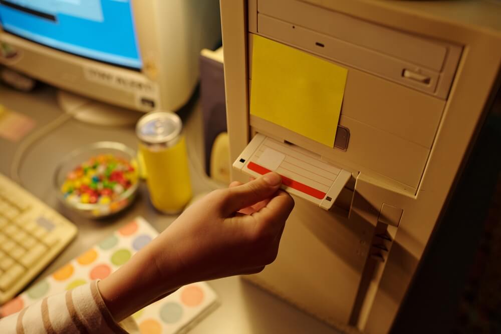 shutterstock_2598320251 mano di persona inserisce floppy disk in vecchio computer il floppy disk rappresenta una delle storiche icone digitali dei computer