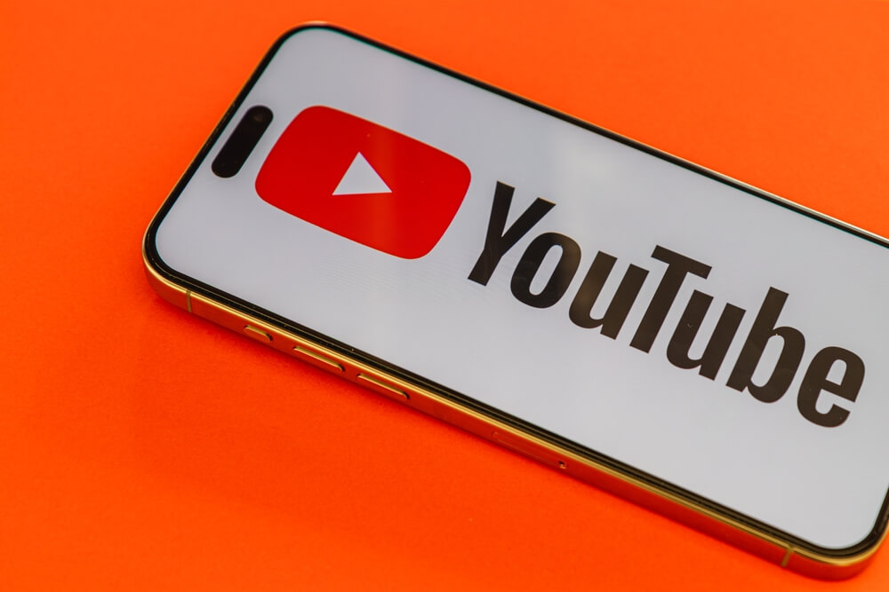 shutterstock_2605372395 logo youtube sullo schermo di uno smartphone su sfondo arancione per rappresentare il nuovo sistema di etichette ai su youtube
