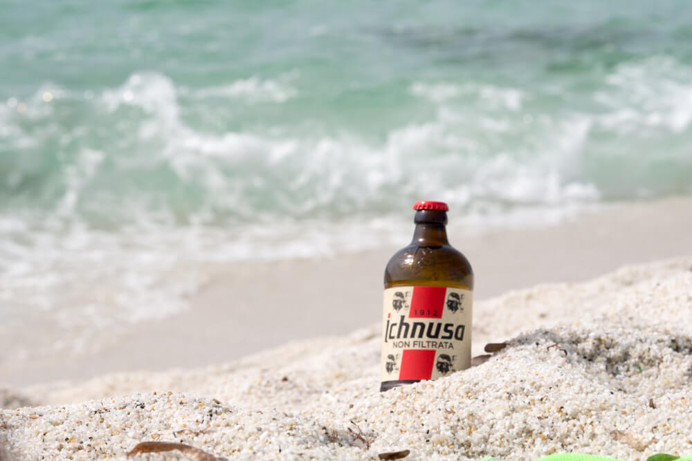 shutterstock_1138453565 bottiglia di birra ichnusa nella sabbia di una spiaggia per rappresntare la campagna metodo lento ichnusa