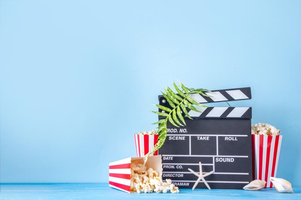 shutterstock_2617628439 ciak su sfondo blu circondato da pop corn alghe e stelle marine conchiglie per rappresentare film digital marketing ai design