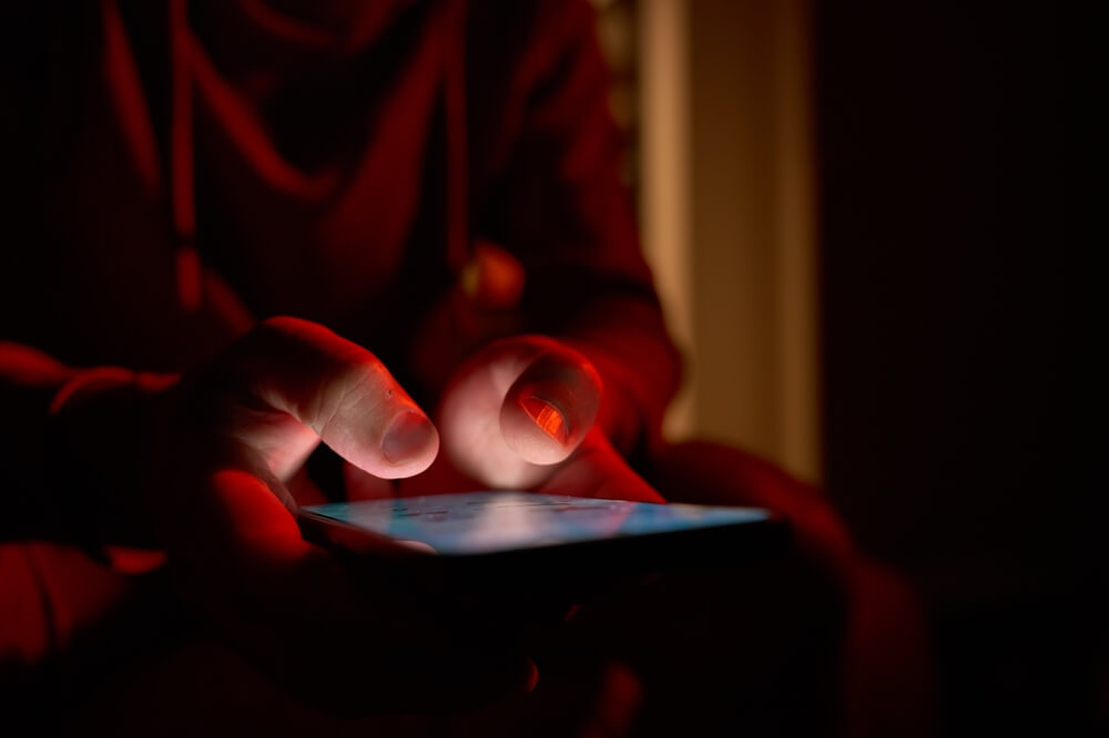 shutterstock_2678218063 mani di uomo mentre usa al buio smartphone per rappresentare perché non riusciamo a smettere di scrollare sui social